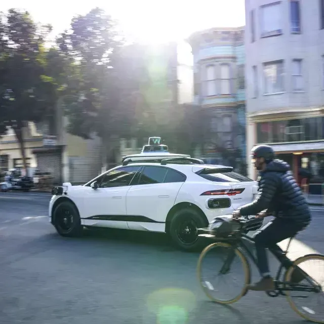 Person riding a bicycle behind a Waymo car